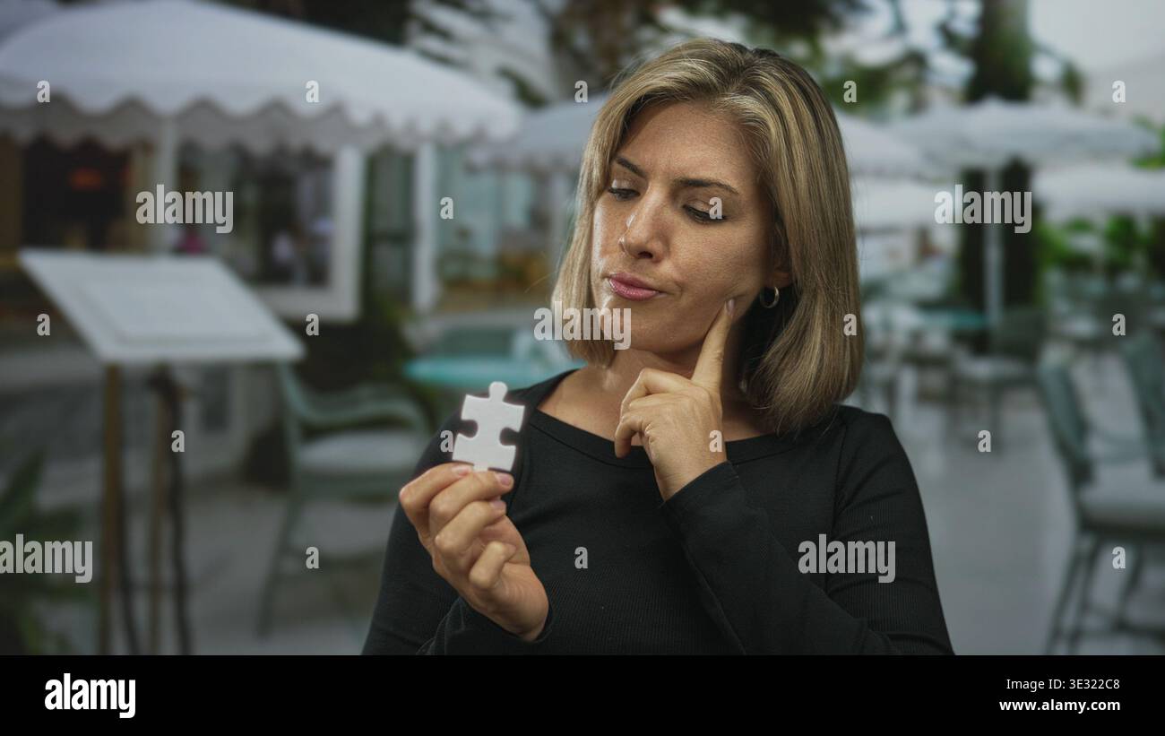 Junge blonde Frau hält weißes Puzzleteil mit Finger auf Wange in einem modernen Restaurantgebäude; Neugier. Stockfoto