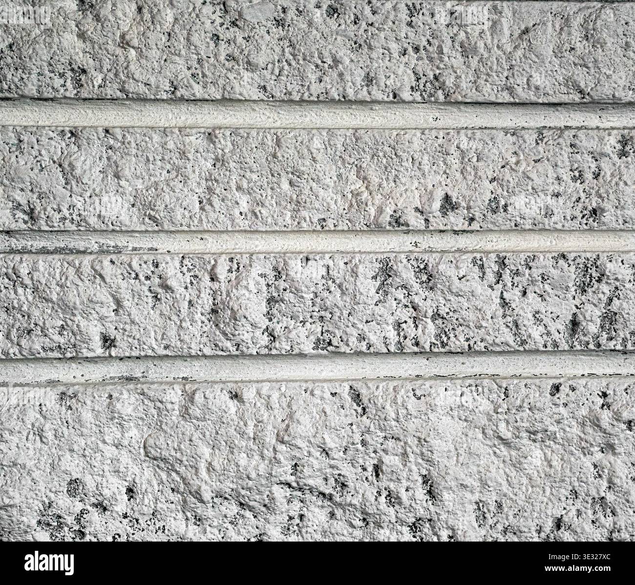 Nahaufnahme einer weißen strukturierten Ziegelwand mit horizontalen Mörtellinien und einer rauen, unebenen Oberfläche mit dunklen gesprenkelten Details. Stockfoto