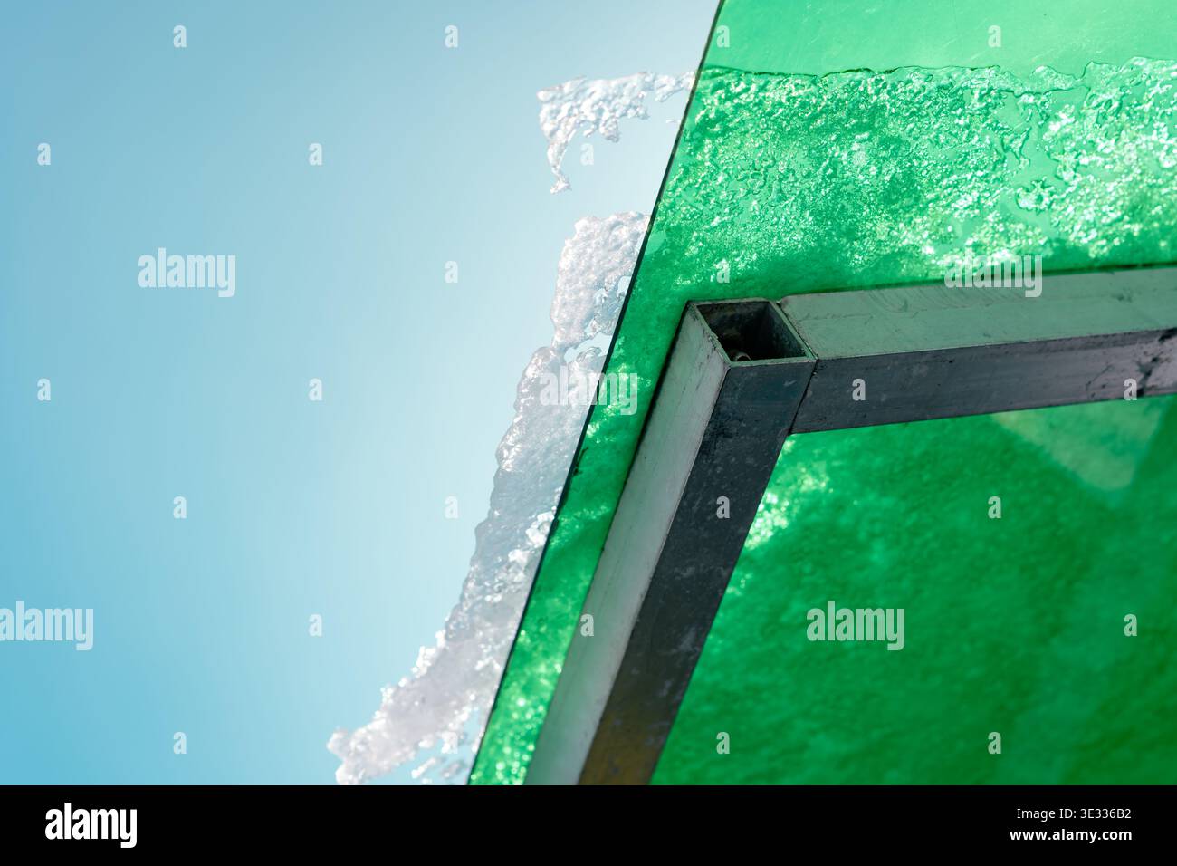 Eine Nahaufnahme aus mattiertem grünem Glas und Metallrahmen vor einem kühlen blauen Hintergrund Stockfoto