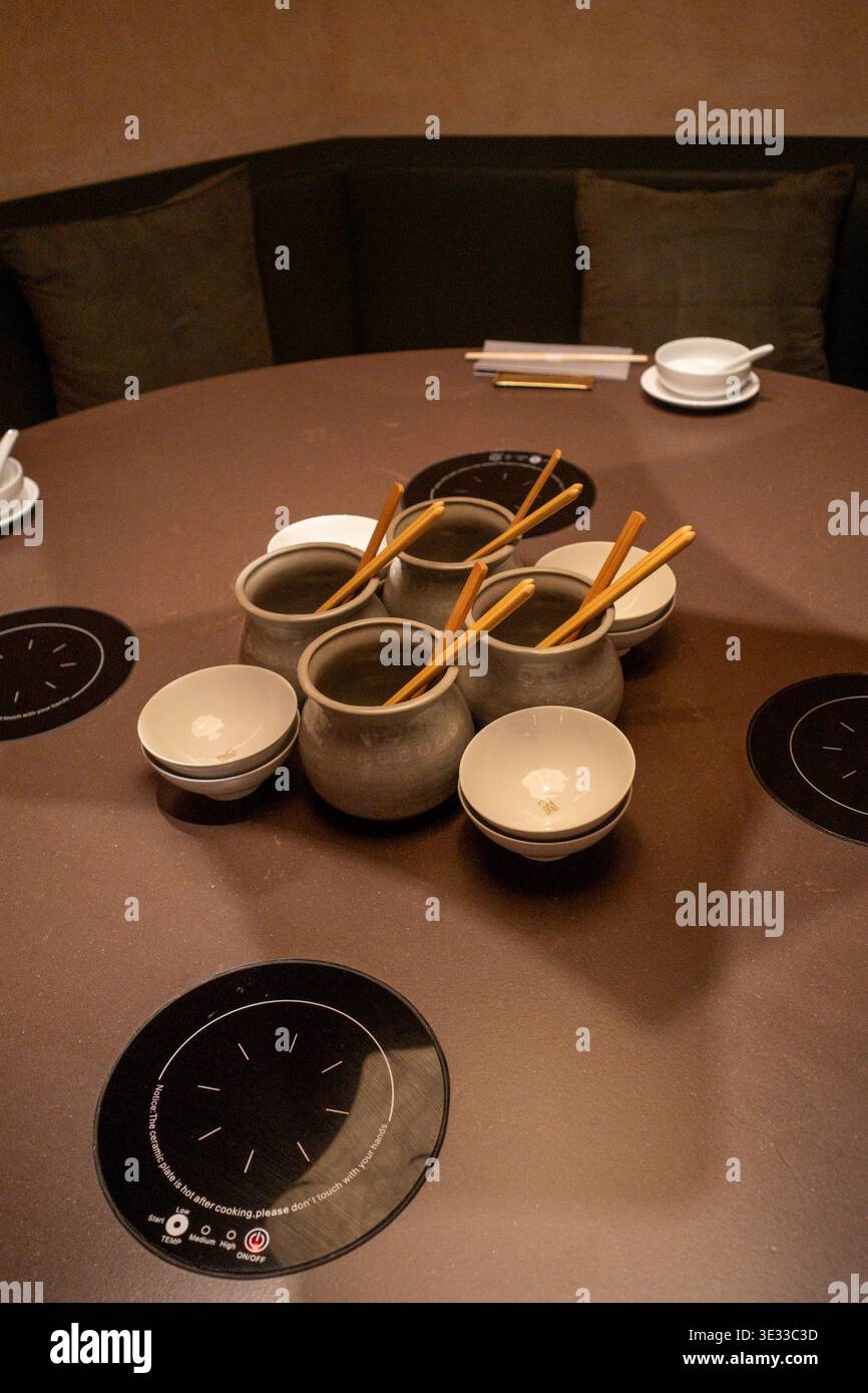 Runder Tisch mit Keramikschalen, Essstäbchen und Einsätzen für Heizplatten. Dunkle Töne sorgen für eine intime Atmosphäre. Edelstahleinsatz sitzt zentriert Stockfoto