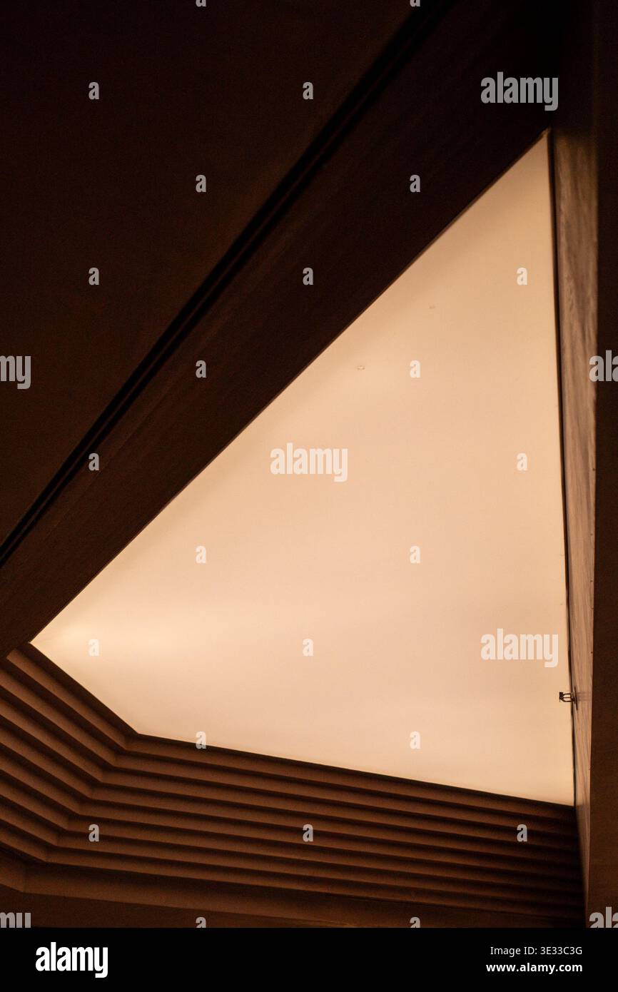 Durch die dreieckige Deckenöffnung leuchtet warmes Licht. Holzbalken bilden weiche, diffuse Beleuchtung. Geometrische Linien erzeugen moderne architektonische Kontur Stockfoto