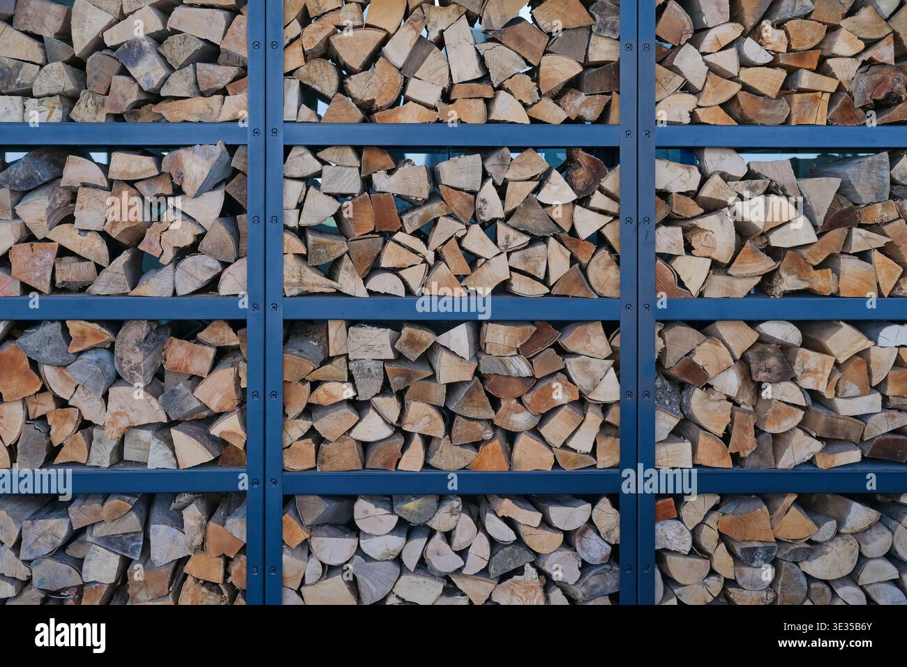 In einer Metallkonstruktion angeordnetes Brennholz. Natürlicher Holzhintergrund mit geometrischem Muster, rustikalem und organischem Materialkonzept. Stockfoto