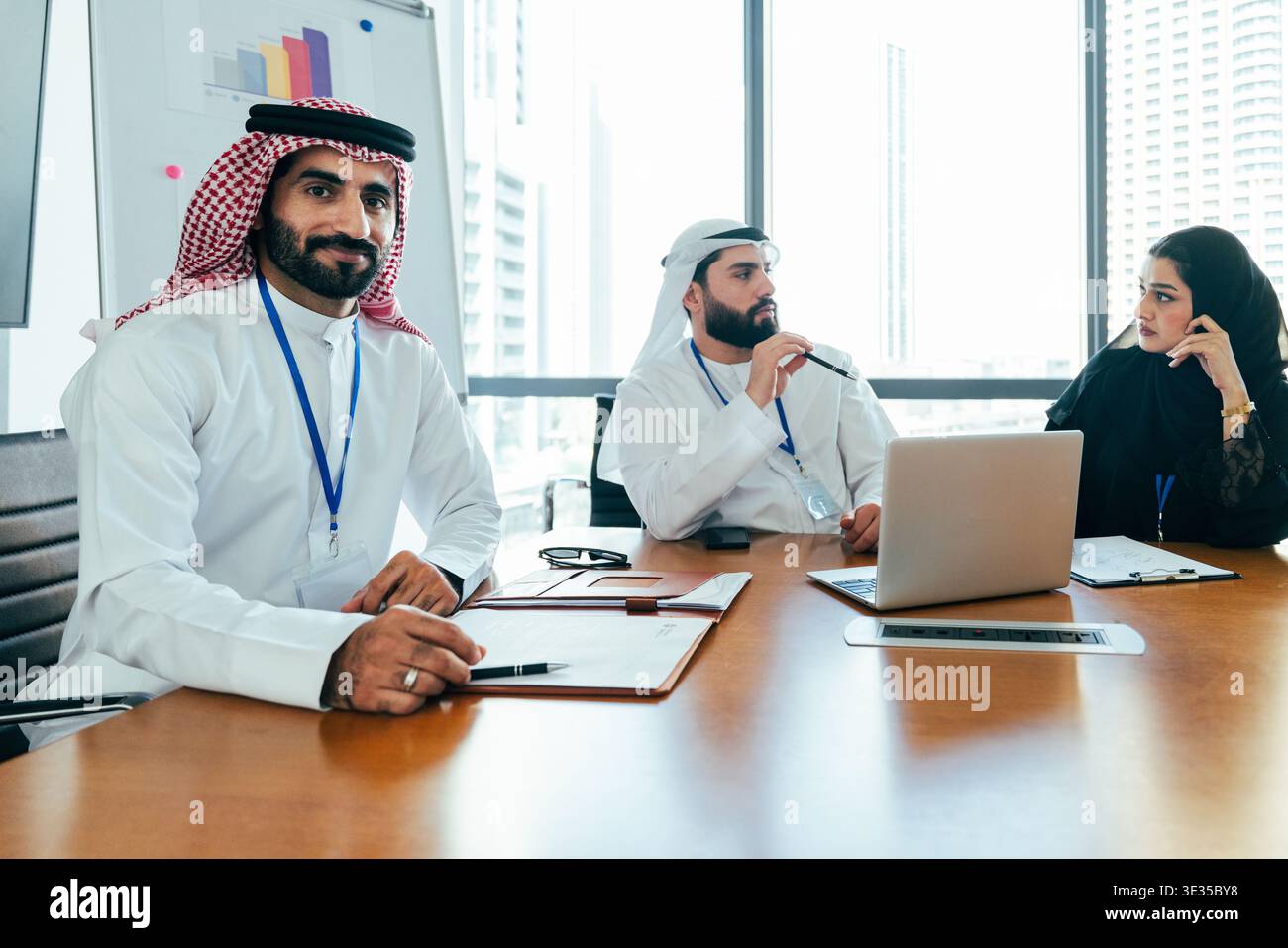 Arabische Geschäftsleute, die in einem modernen Büro ein Meeting mit Schwerpunkt auf Teamarbeit, Kommunikation und globaler Strategie mit einem Stadtbild veranstalten Stockfoto