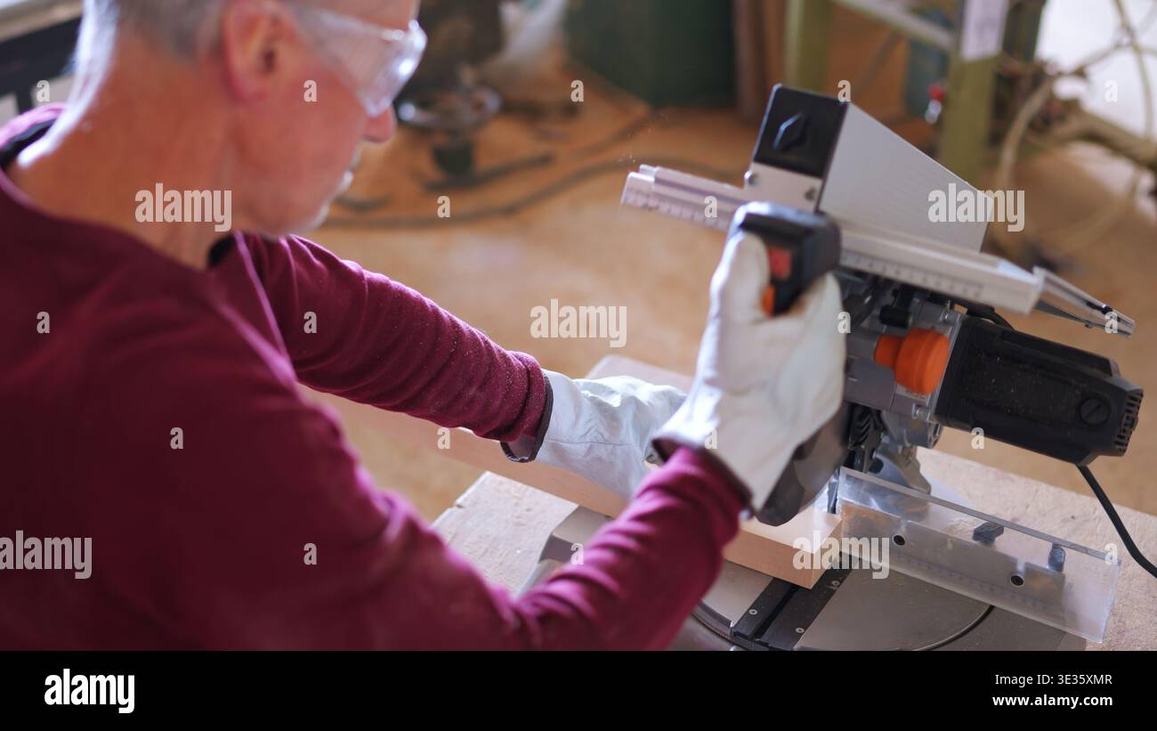 Zimmermann schneidet Holz mit Gehrungssäge mit Schutzbrille Stockfoto