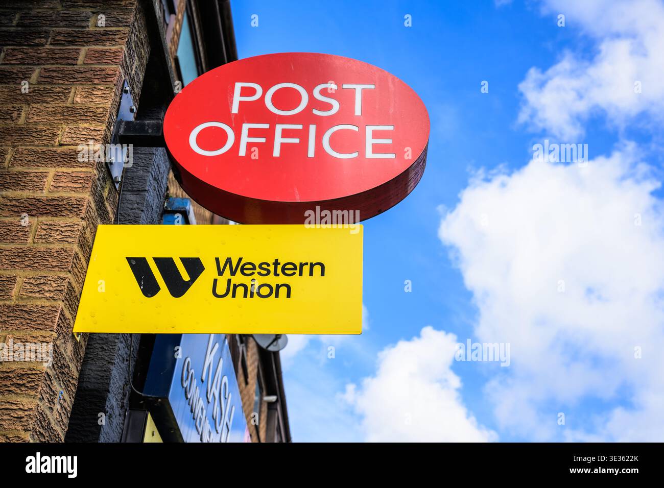 Rotes Postamt-Schild, das über einem gelben Western Union-Schild an der Außenfassade des Gebäudes angebracht ist und Postdienste und internationalen Geldtransfer darstellt. Stockfoto