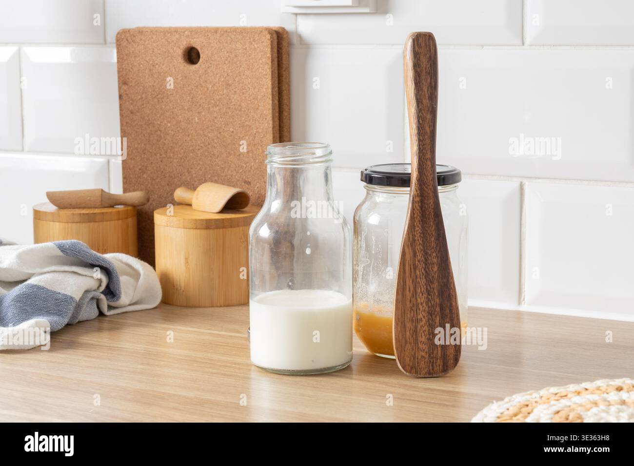 Eine saubere Küchenzeile mit Milch, geschmolzener Butter, Gläsern mit Salz, Holzutensilien und einem Tuch, bereit zum Kochen. Stockfoto