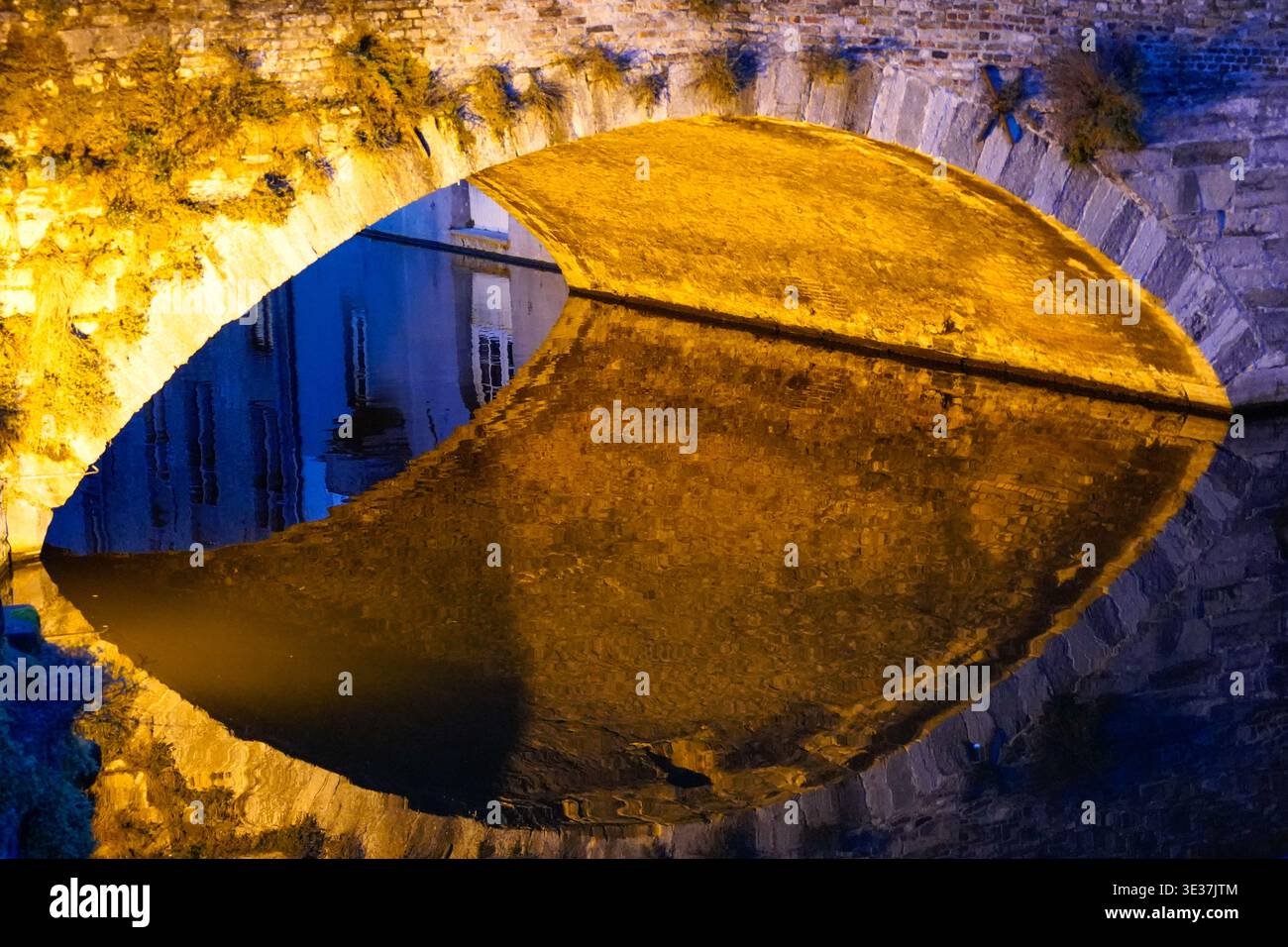 Beleuchtete Stone Arch Bridge, die nachts auf dem Wasser reflektiert wird Stockfoto