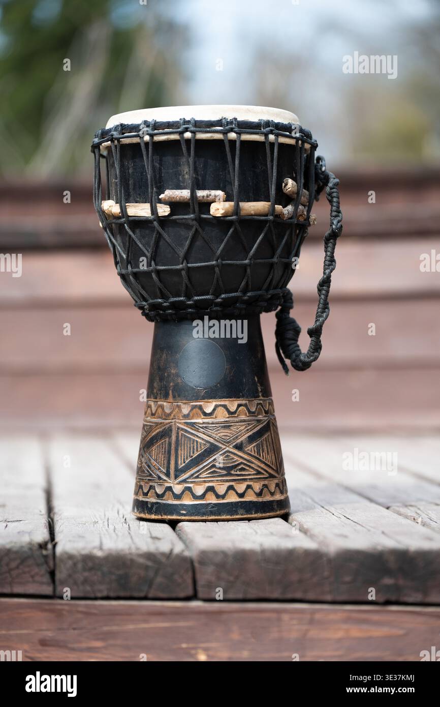 Traditionelle afrikanische Djembe-Trommel auf einer Holzterrasse. Handgeschnitztes Schlaginstrument mit ethnischen Mustern und schwarzem Finish. Stockfoto