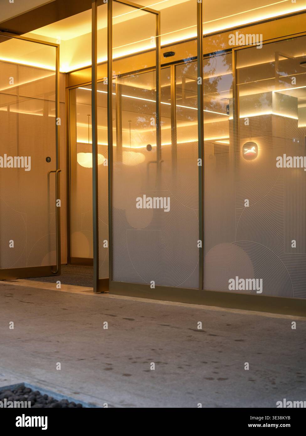 Eingang eines modernen Geschäftsgebäudes mit Glastüren und Mattpaneelen, beleuchtet durch warmgelbes Licht bei Nacht. Die Szene repräsentiert Upscal Stockfoto