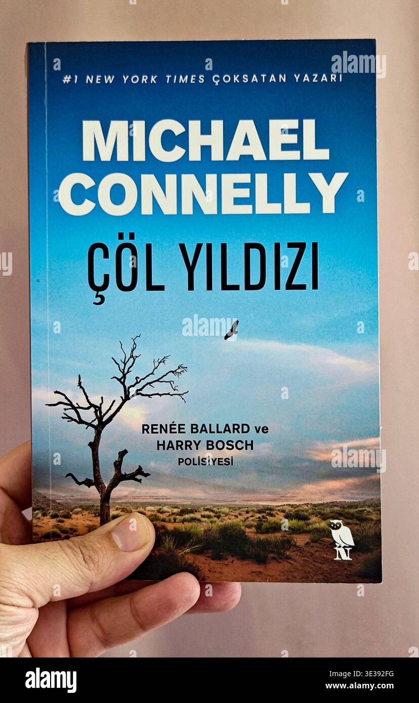 Hand hält eine türkische Taschenbuchausgabe von Michael Connellys Kriminalthriller „Desert Star“ (Cöl Yıldızı) vor einem einfachen Hintergrund. Stockfoto