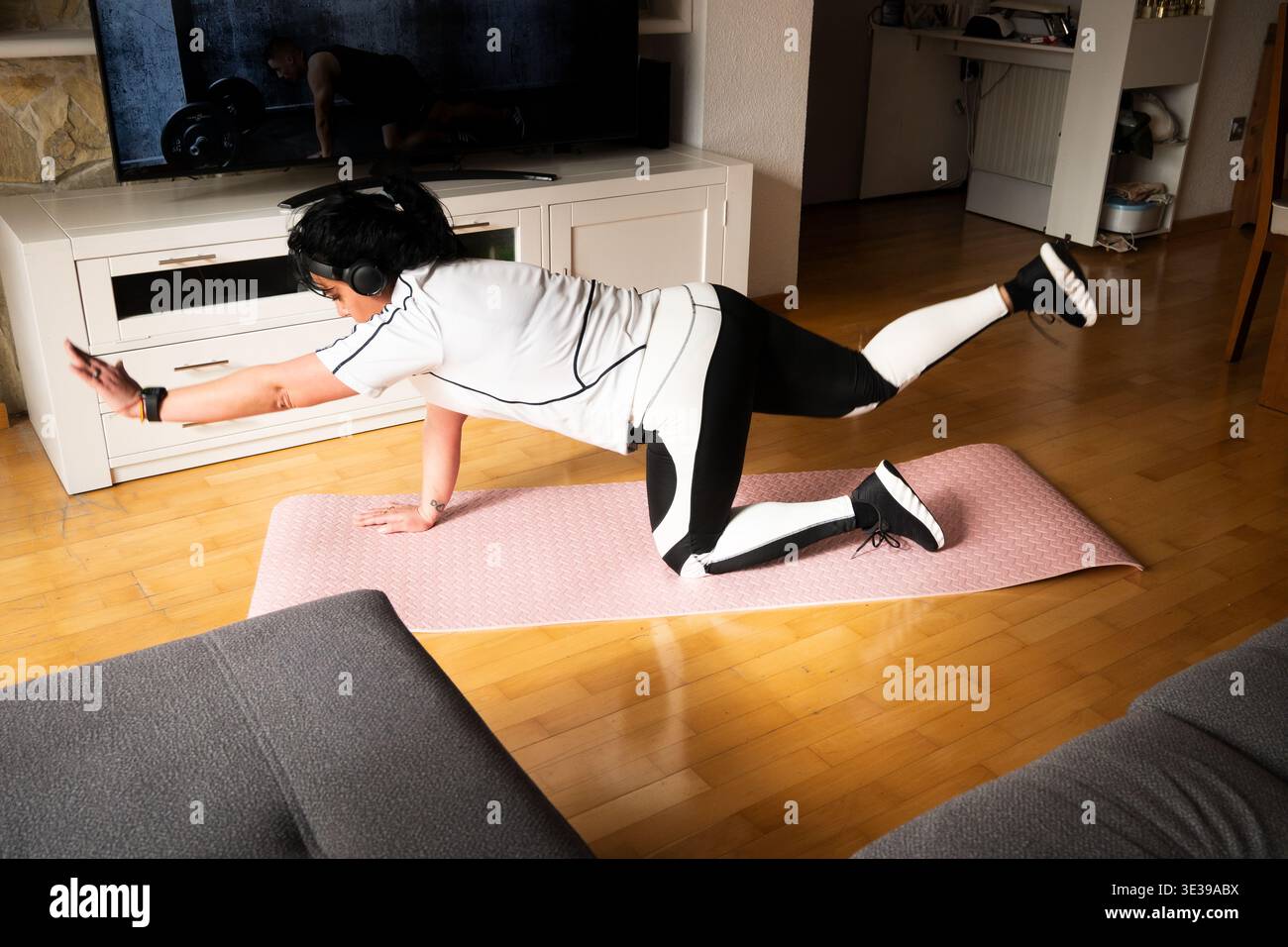 Frau, die Vogelhund-Übungen auf einer Yogamatte im Wohnzimmer durchführt Stockfoto