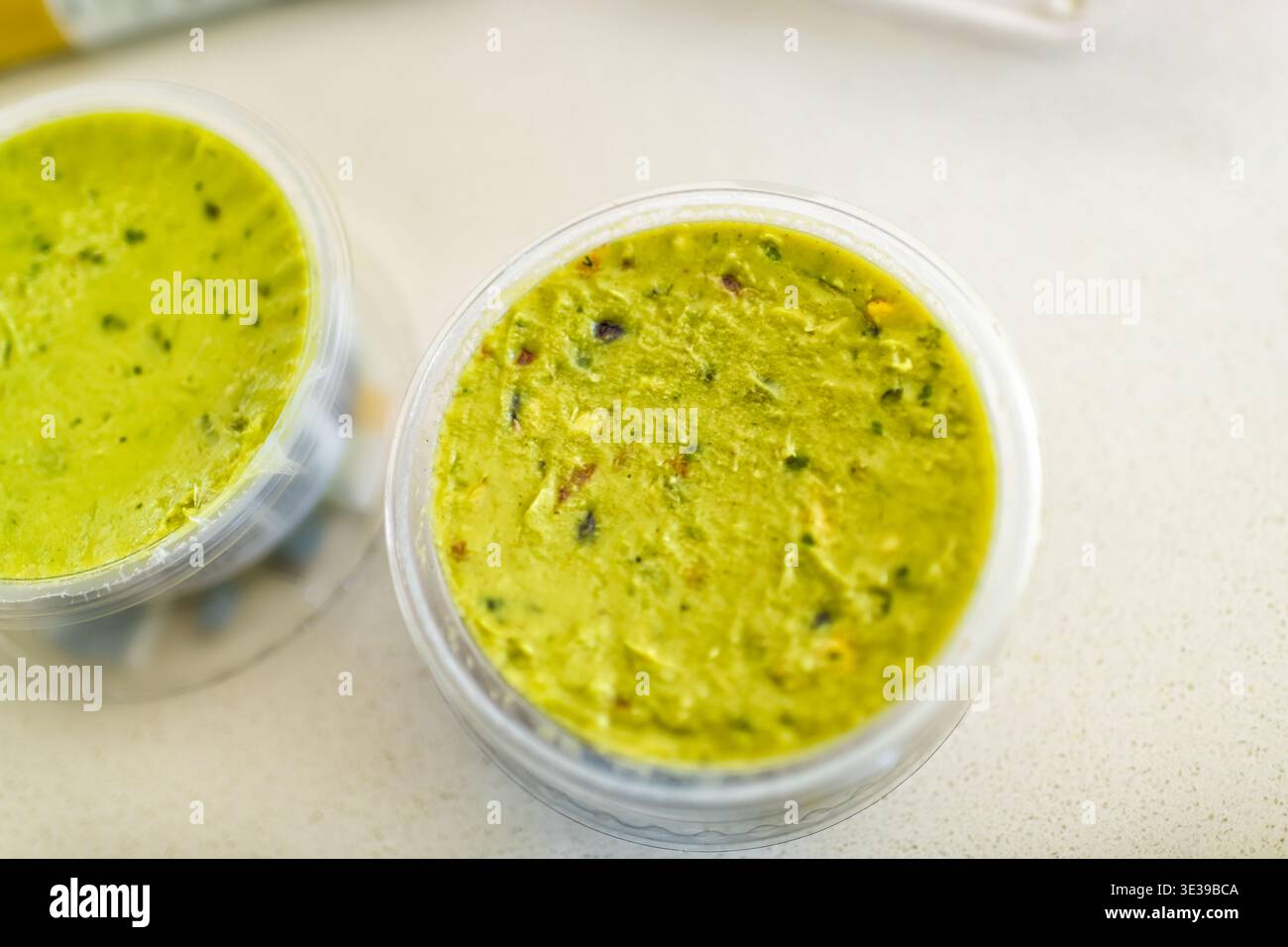 Plastikbehälter Schüssel Becher mit Bio-grünem Guacamole-Geschmack mit Löffel, die Nahaufnahme mit gemahlenen Avocados, Tomaten, Knoblauch und Gemüse servieren Stockfoto