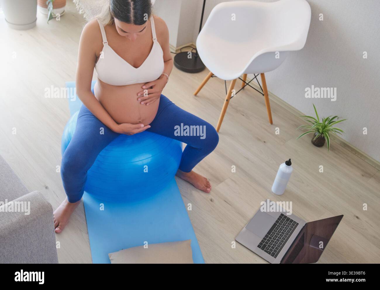 Erwartende Mutter macht Schwangerschaftsübungen auf einem blauen Fitball in ihrem Wohnzimmer für einen gesunden Lebensstil Stockfoto