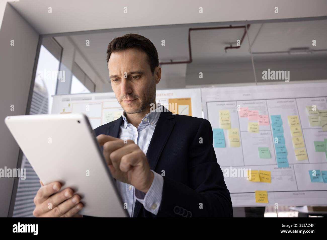 Konzentrierter Millennial-Geschäftsmann im formellen Anzug analysiert Informationen mit Tablet Stockfoto