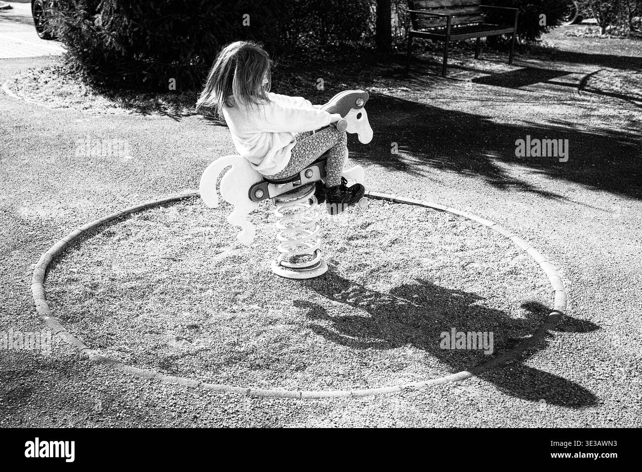 Schwarz-weiß-Foto eines Kindes, das auf dem Spielplatz des Frühlingsreiters spielt. Kreative Szene mit starkem Schatten, die dynamische Form bildet und die Fantasie symbolisiert Stockfoto