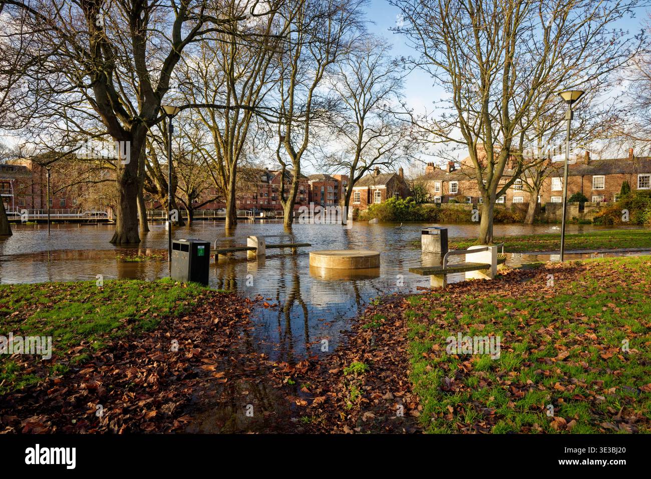 Ein Pfad führt durch einen Stadtpark zu einem überfluteten Gebiet durch einen Fluss mit Häusern im Hintergrund, City of York, England. Stockfoto