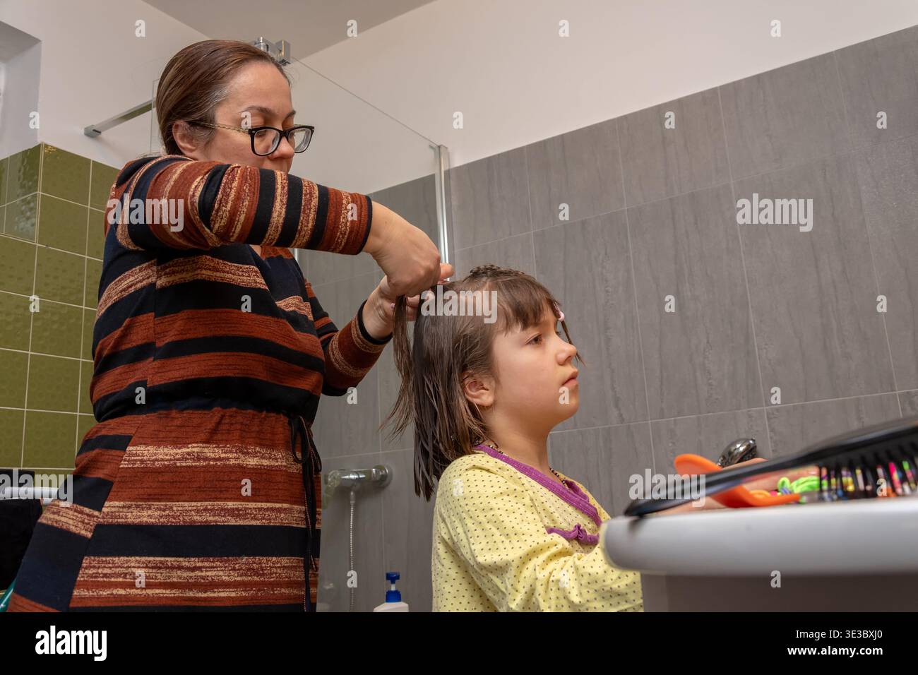 Die Frau kreiert eine ordentliche Frisur für das Kind nach dem Waschen vor Tagesbeginn Stockfoto