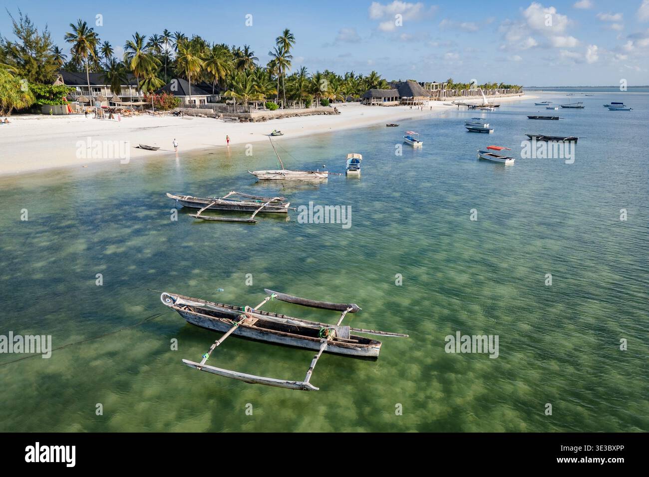 Blick aus der Vogelperspektive auf traditionelle Holzboote, die in klarem türkisfarbenem Wasser an einem tropischen weißen Sandstrand mit Palmen und Resorts ankern. Ort: Zan Stockfoto