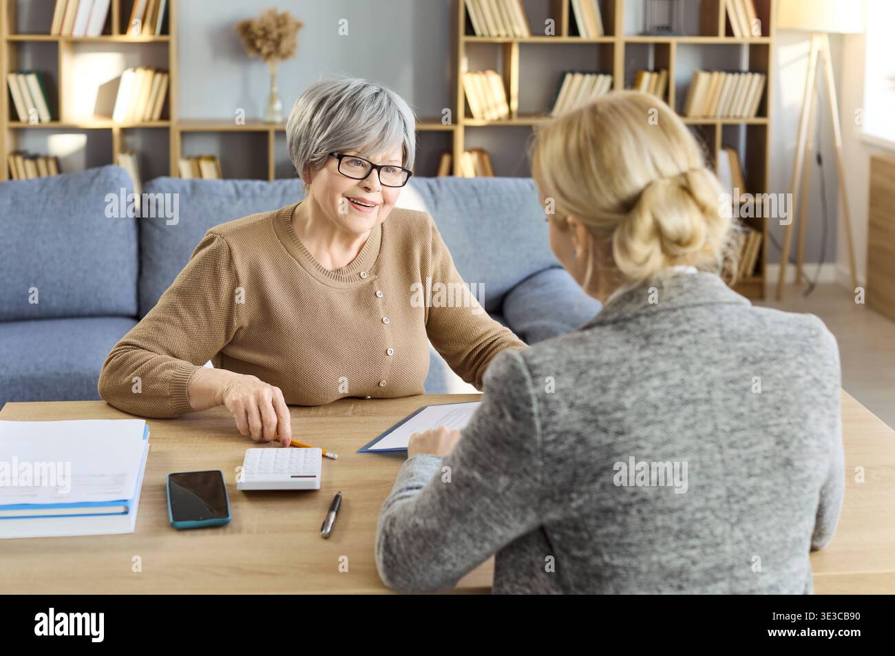Zufriedener Senior Client, der Finanzen mit weiblicher Beraterin zu Hause diskutiert Stockfoto