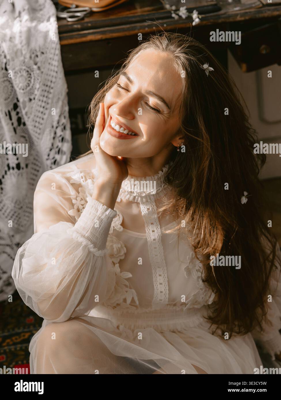 Traumhaftes, sonnendurchflutetes Porträt einer jungen Frau in Spitzenkleid, sanftem Lächeln und romantischer Vintage-Stimmung. Stockfoto