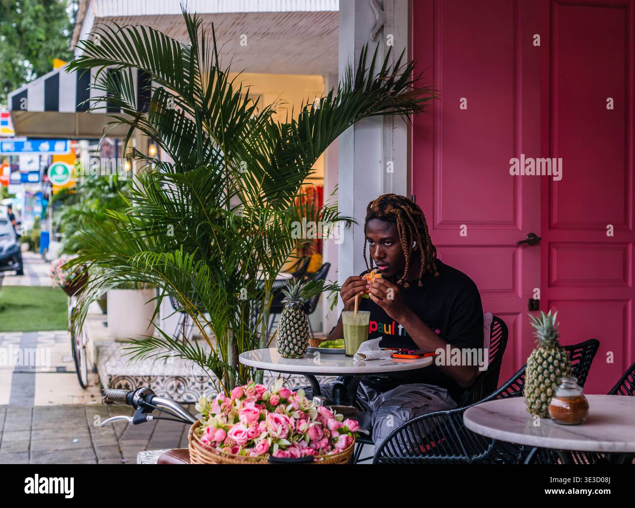 Junger Mann, der in einem hellen Pink Outdoor Cafe isst Stockfoto