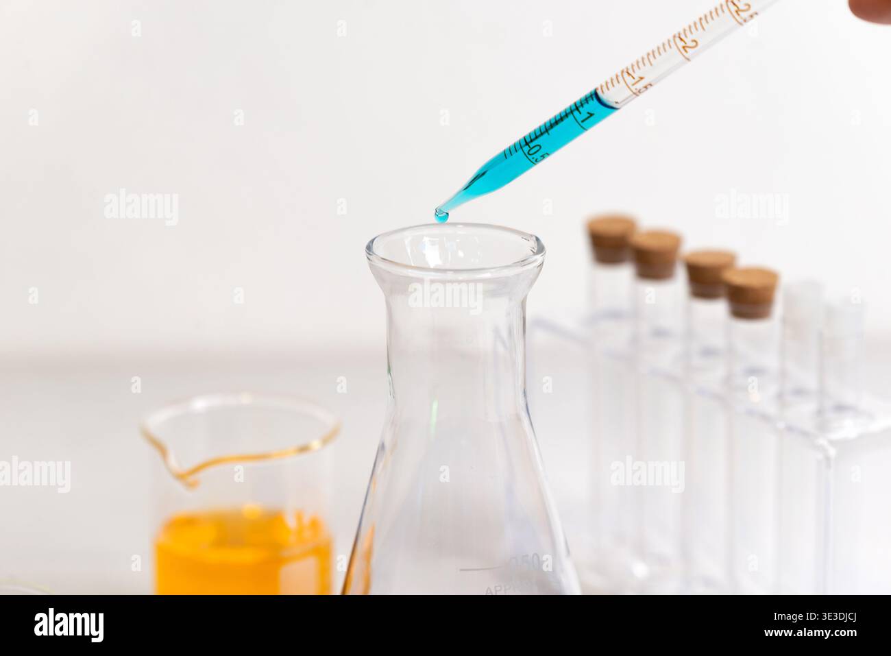 Tropfen der blauen Flüssigkeit in den Laborkolben für präzise chemische Messungen, wissenschaftliche Forschung und Labortests Stockfoto