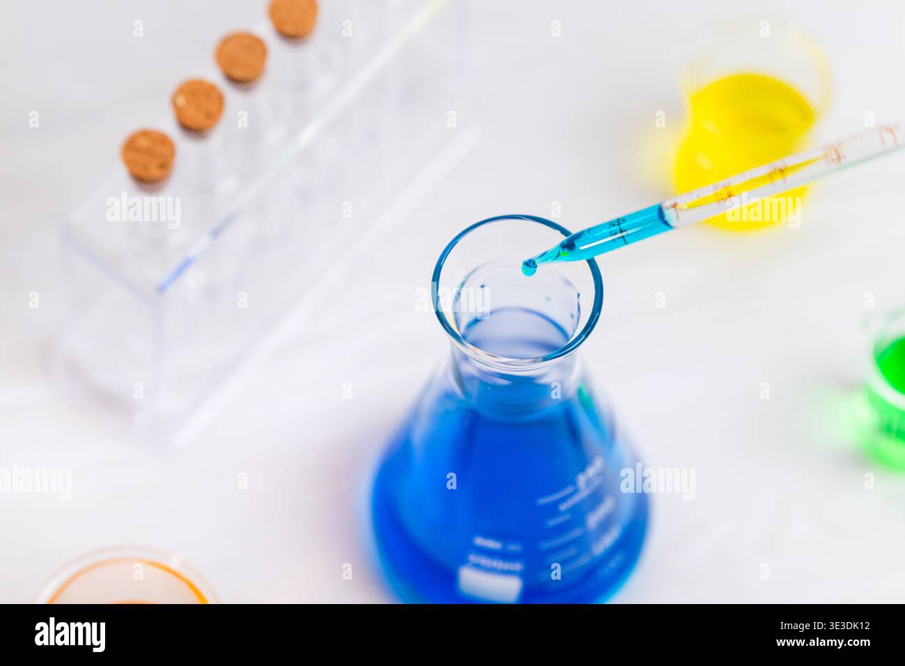 Pipette mit Flüssigkeitstropfen über dem Laborkolben mit Reagenzgläsern im Hintergrund für medizinische Forschung und chemische Analyse Stockfoto