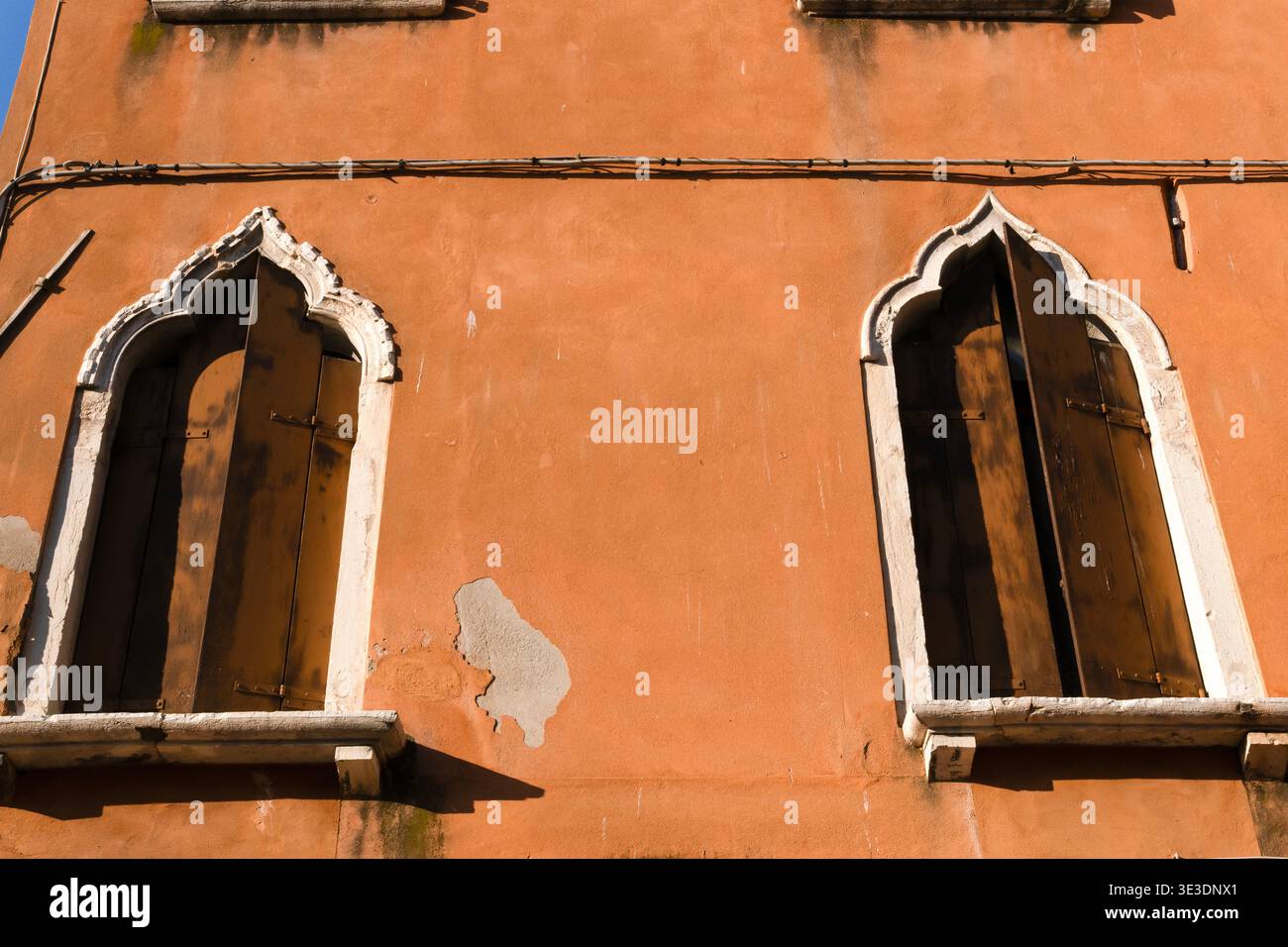 Typische antike venezianische Fenster mit gotischen Bögen und dunklen Holzläden und Steinfensterbänken in einer orangen Wand. Venedig, Italien Stockfoto