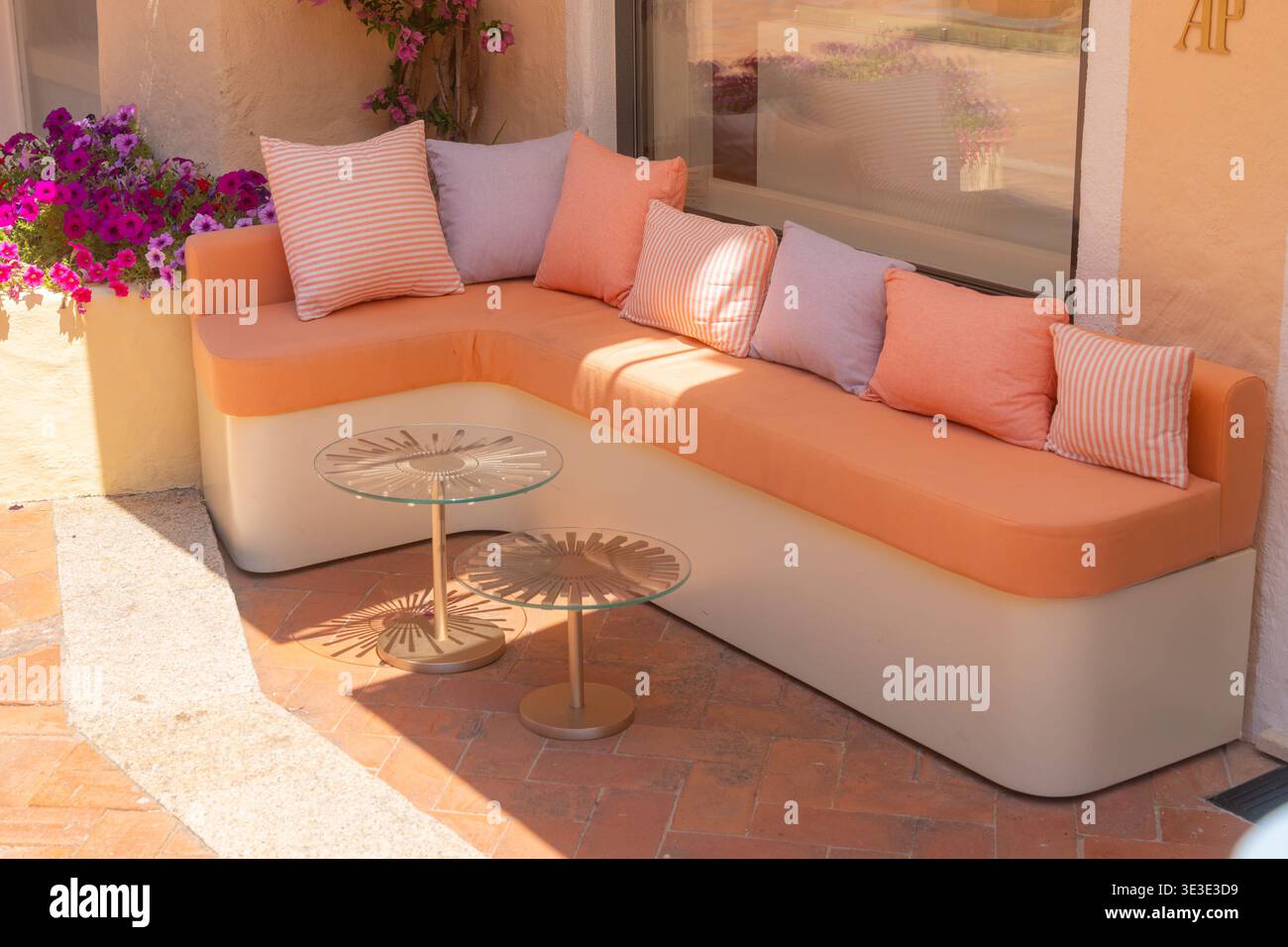 Stilvolle Lounge im Freien mit weichem Sofa, Kissen und Blumen. Luxuriöses Terrassendesign und Sommerentspannungskonzept Stockfoto