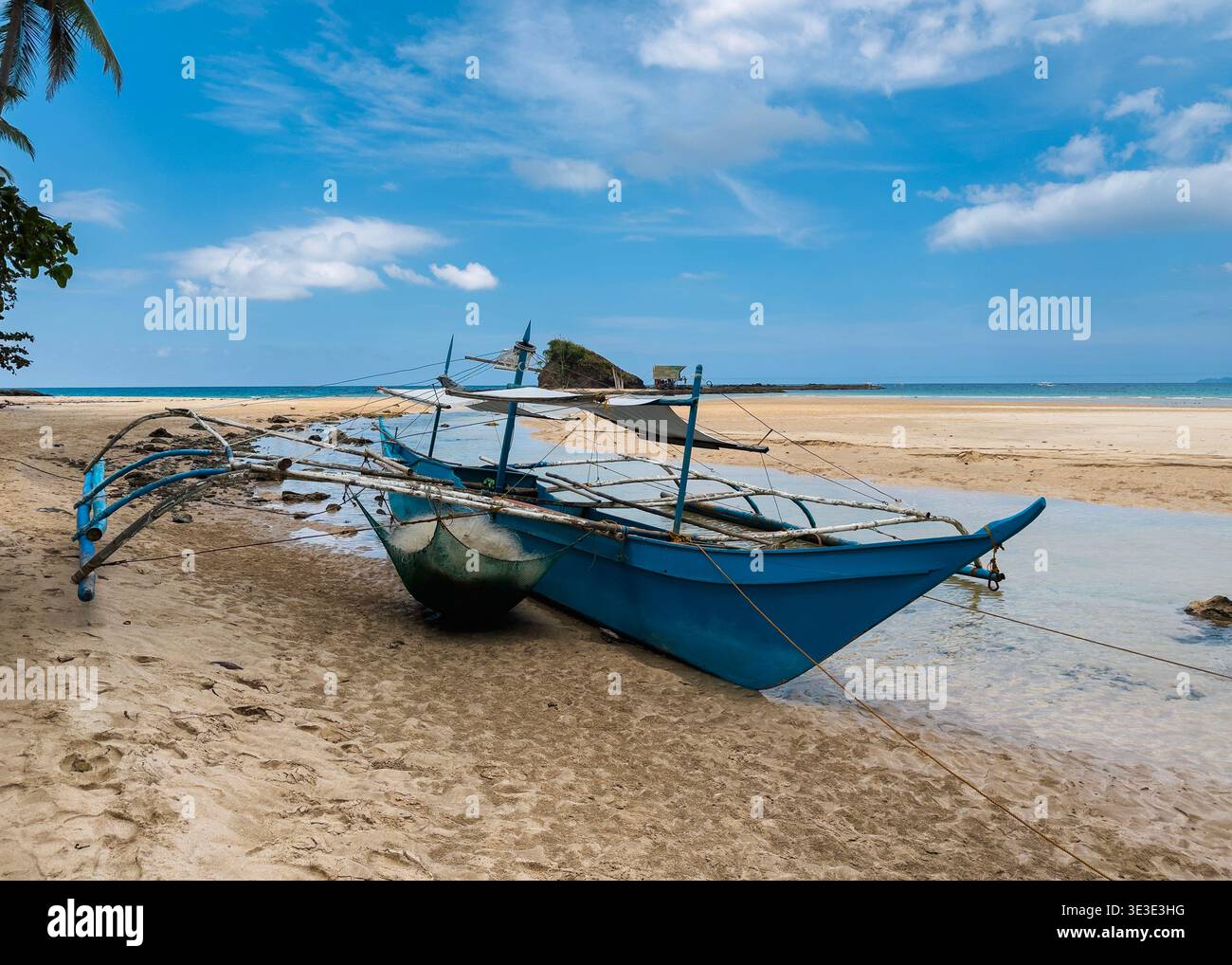 Das traditionelle Auslegerboot liegt am Sabang Beach, Puerto Princesa, Palawan, Philippinen, mit ruhigem Wasser und sandiger Küste unter tropischem Himmel. Stockfoto