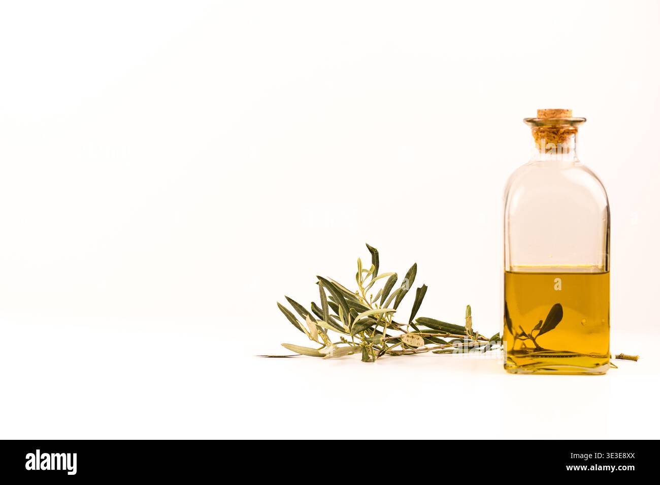 Glasflasche Olivenöl mit Olivenzweig isoliert auf weißem Hintergrund mit viel Kopierraum. Stockfoto