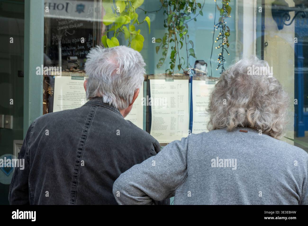 Älteres grauhaariges Paar, das sich die Speisekarte vor einem Restaurant im Stadtzentrum von Bath, Somerset, England, anschaut Stockfoto