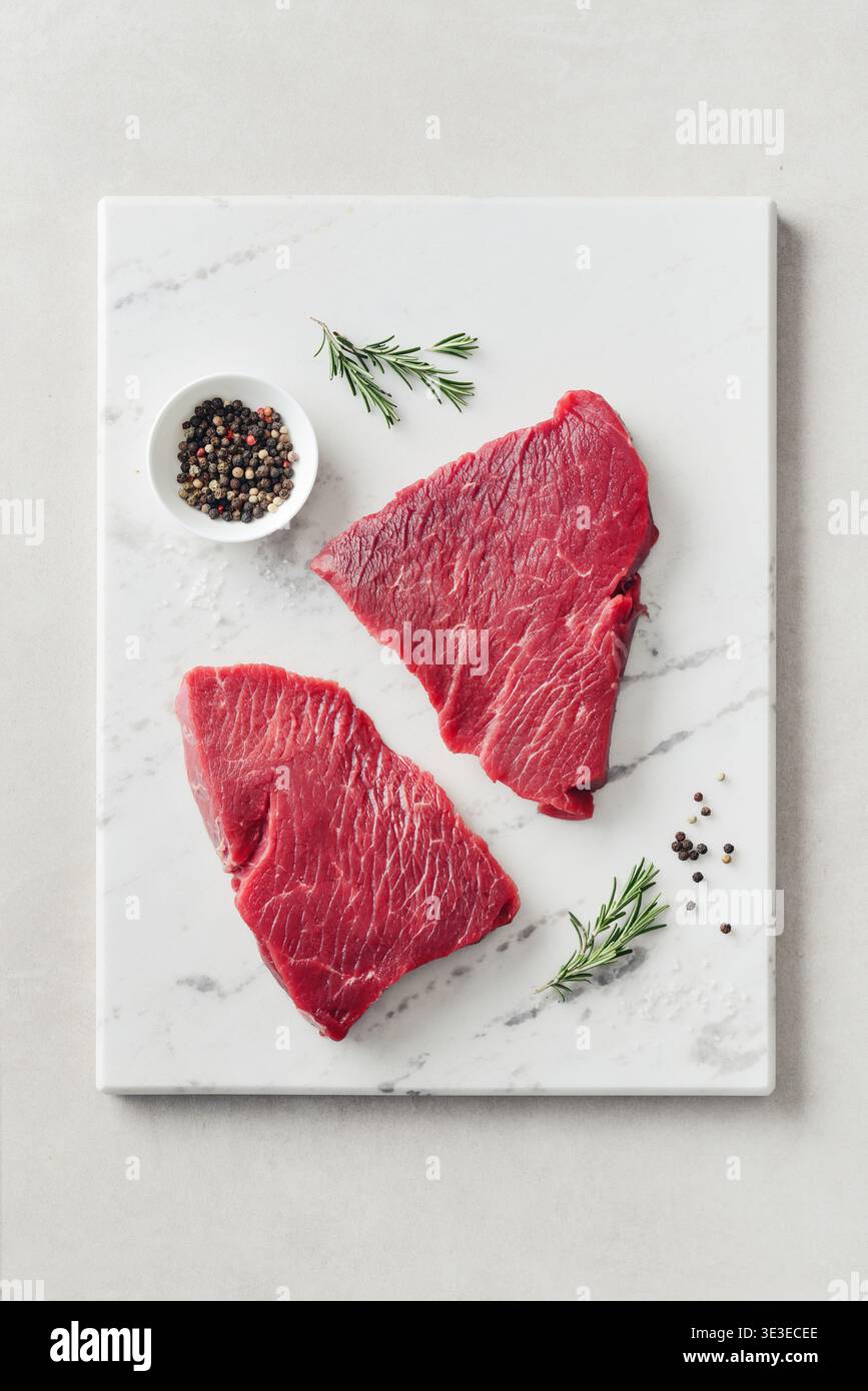 Rohe Rindersteak und Gewürze zum Kochen auf Marmor Schneidebrett auf hellem Hintergrund, Blick von oben Stockfoto