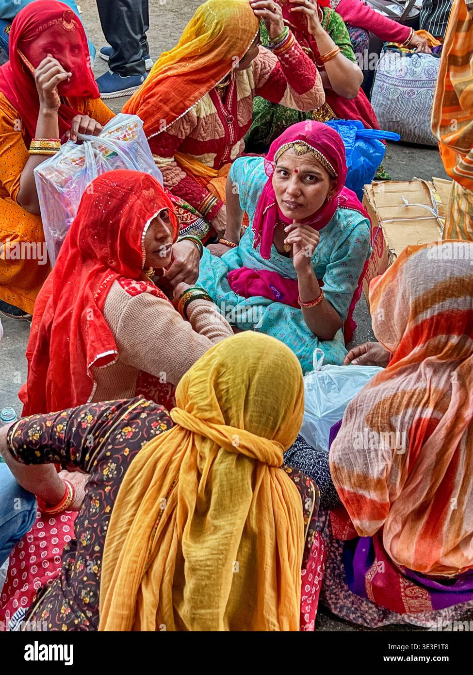 JODHPUR, INDIEN - 30. DEZEMBER 2022: Eine Gruppe unbekannter Frauen in bunten Kleidern sitzt auf der Straße nach dem Einkaufen auf dem Jodhpur Markt und wartet Stockfoto