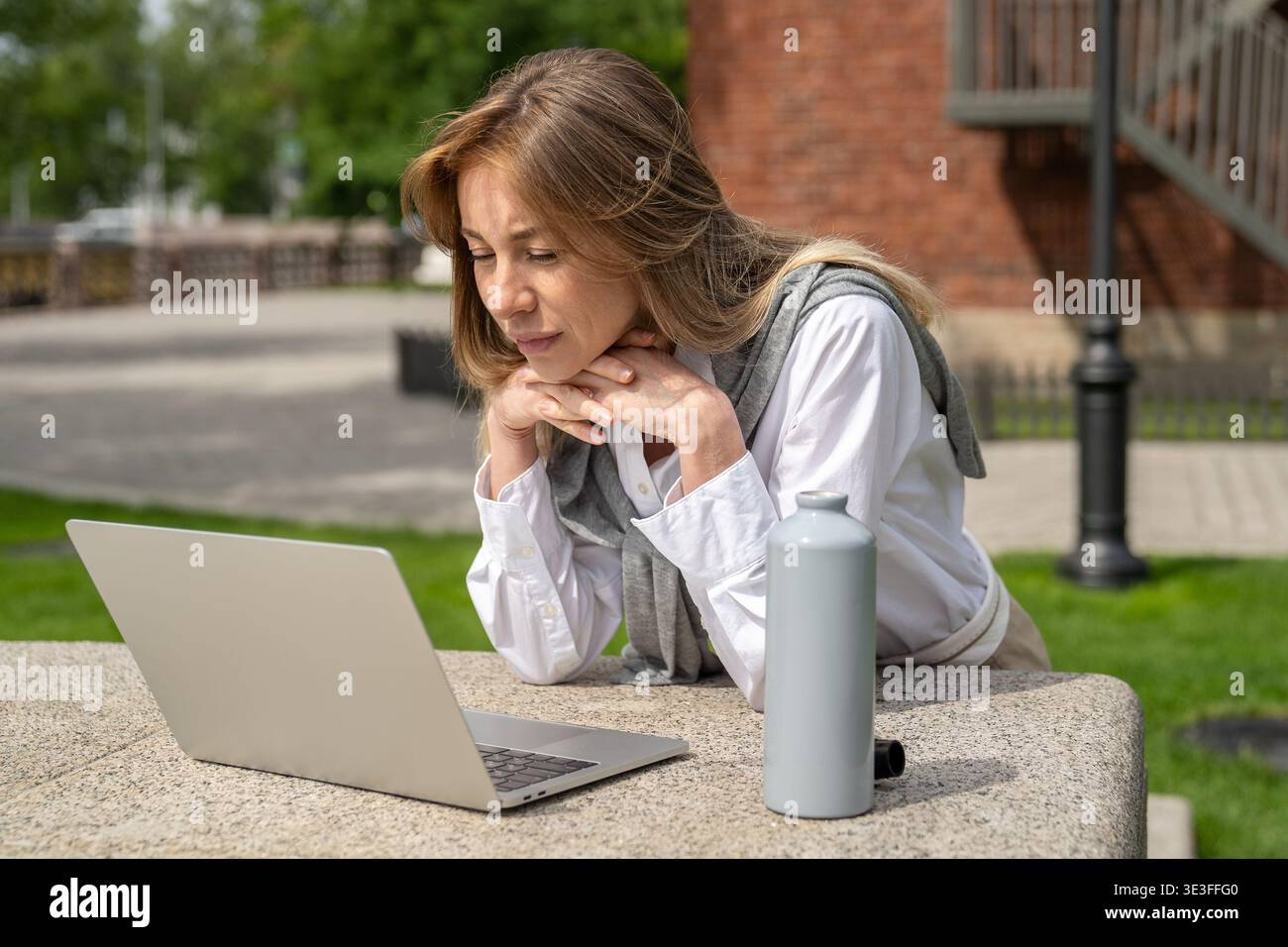 Eine neugierige positive Geschäftsfrau arbeitet im Freien an einem Laptop, eine fokussierte Dame schaut sich das Webinar am Computer an. Stockfoto