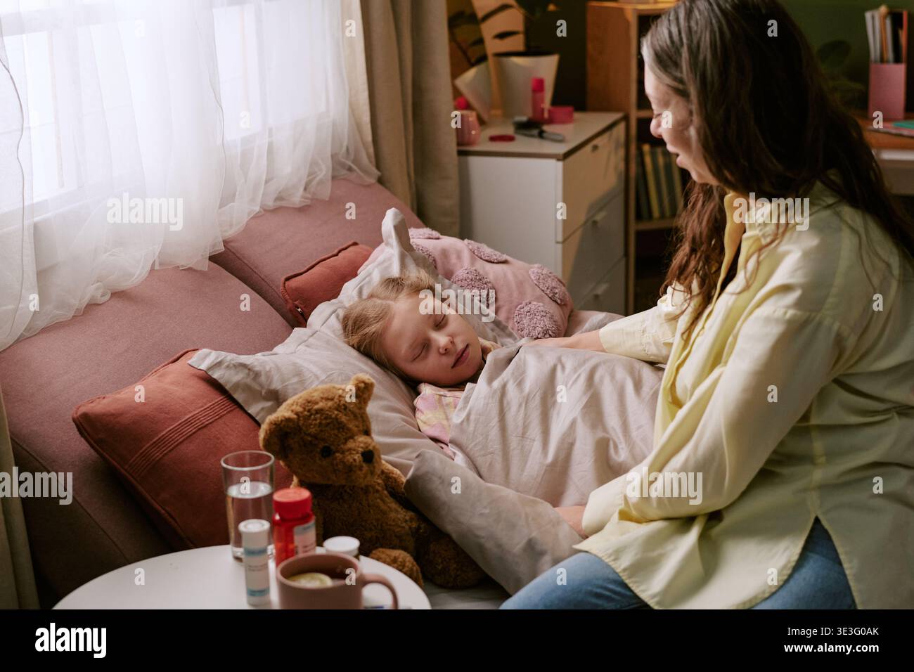Frau mittleren Alters tröstet krankes Kind, das im Schlafzimmer ruht Stockfoto