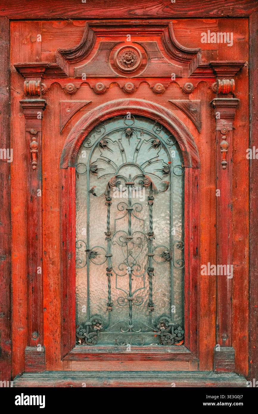 Antik rot lackierte Holztür mit kunstvoll geschnitztem Barockrahmen mit zentraler Rosette, Scrollwerk, dekorativen Konsolen, gedrehten Pilastern und Sp Stockfoto