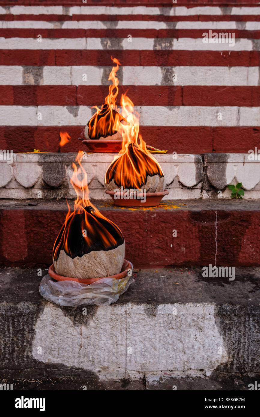 Drei brennende Kokosnüsse befinden sich auf der markanten rot-weiß bemalten Steintreppe von Kedar Ghat in der Stadt Varanasi. Stockfoto