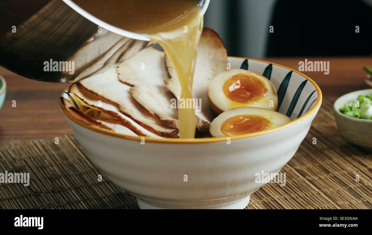 Der Koch gießt heiße herzhafte Brühe in eine Schüssel authentischer japanischer Ramen Stockfoto