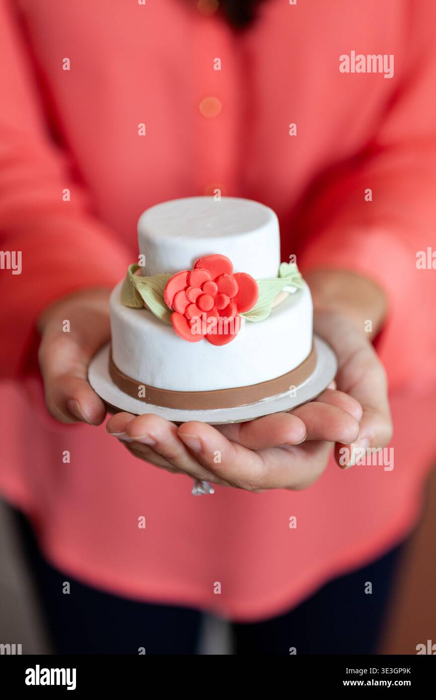 Frau, die einen kleinen verzierten Kuchen mit Blumendetail hält. Stockfoto