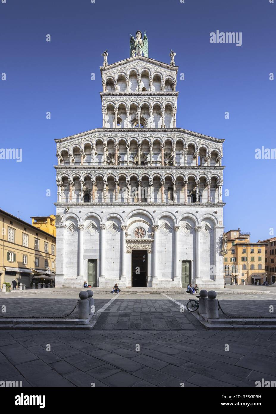 Blick auf die Kirche San Michele in Foro, eine Symphonie aus weißen Marmorschichten, die sich gegen einen klaren blauen Himmel erheben und lange Schatten auf die Kopfsteinpflaster werfen Stockfoto