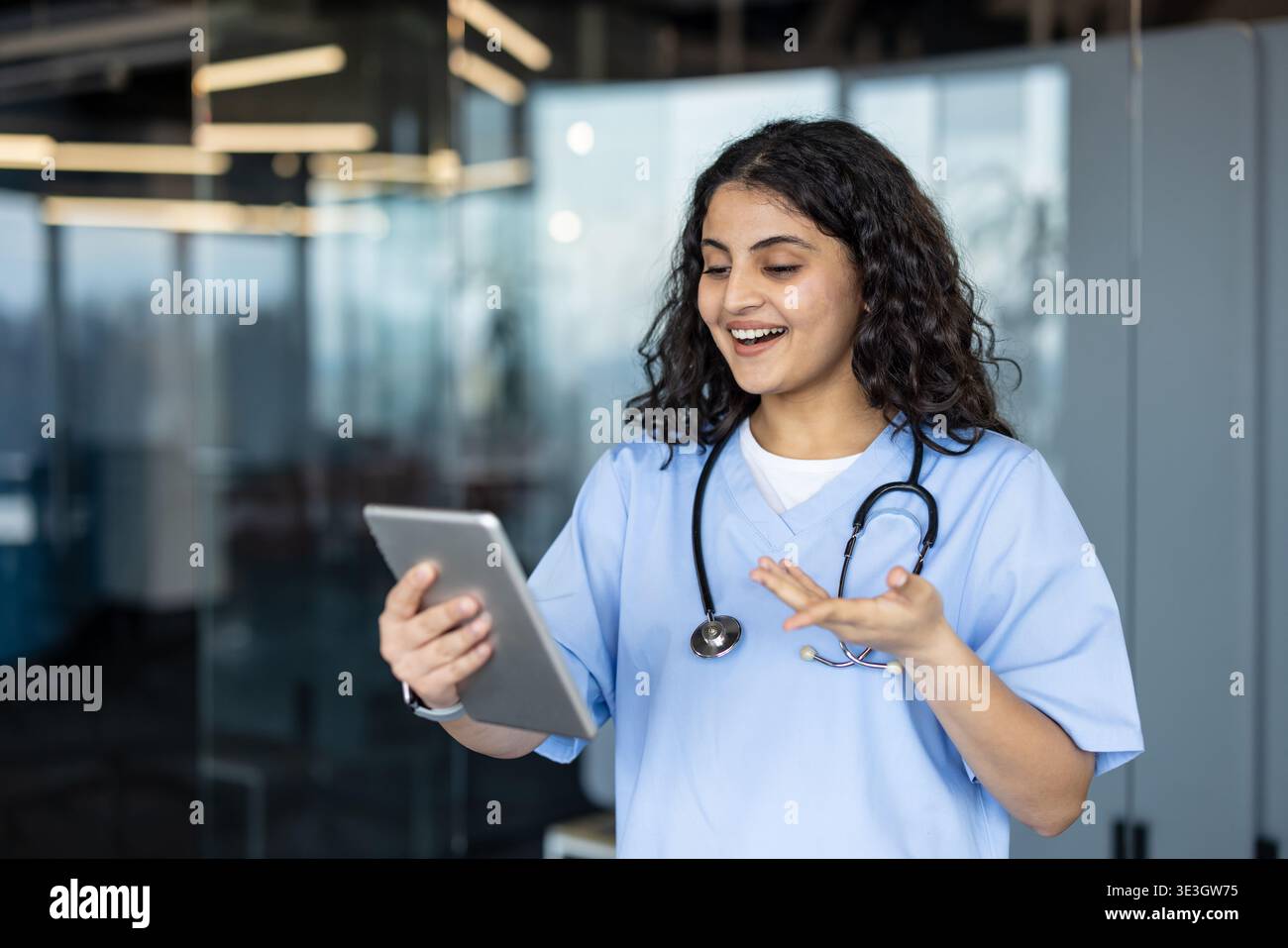 Junge Ärztin oder Krankenschwester in blau schrubbt mit einem digitalen Tablet für eine virtuelle Patientenberatung, kommuniziert und bewegt fröhlich während eines Remote-Arzttermins Stockfoto
