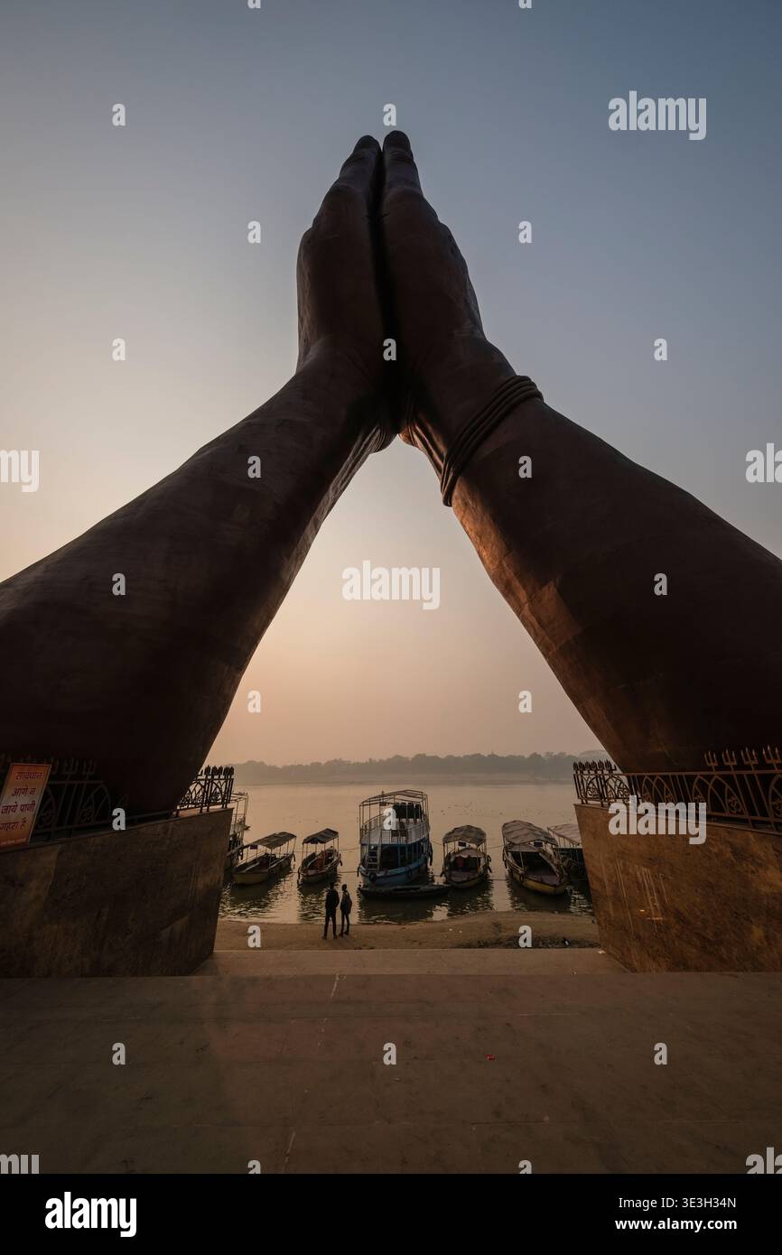 Eine niedrige Ansicht zeigt die Namo Mudra Hände am Namo Ghat in Varanasi, die mehrere Boote umrahmt, die bei Sonnenaufgang am Ganges angedockt sind. Stockfoto