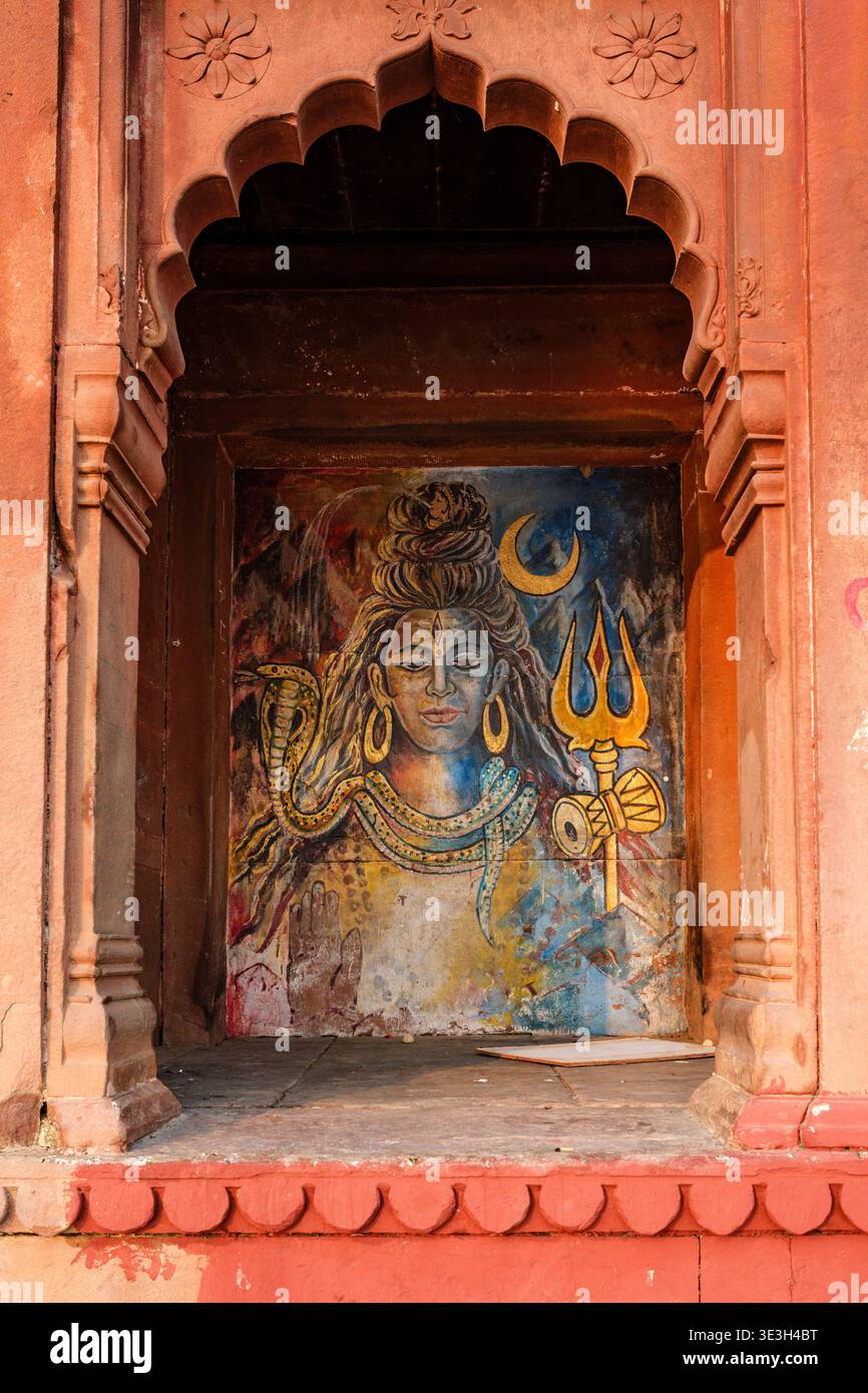 Ein detailliertes Wandbild der hinduistischen Gottheit Shiva befindet sich in einer dekorativen bogenförmigen Steinnische in einem der vielen alten Ghats, die in Varanasi gefunden wurden. Stockfoto