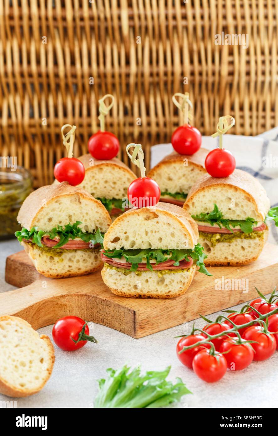 Baguette-Sandwiches mit Pesto-Sauce, Wurst oder Schinken, Käse, Salat und Kirschtomaten. Picknick-Essen. Selektiver Fokus, Kopierraum Stockfoto