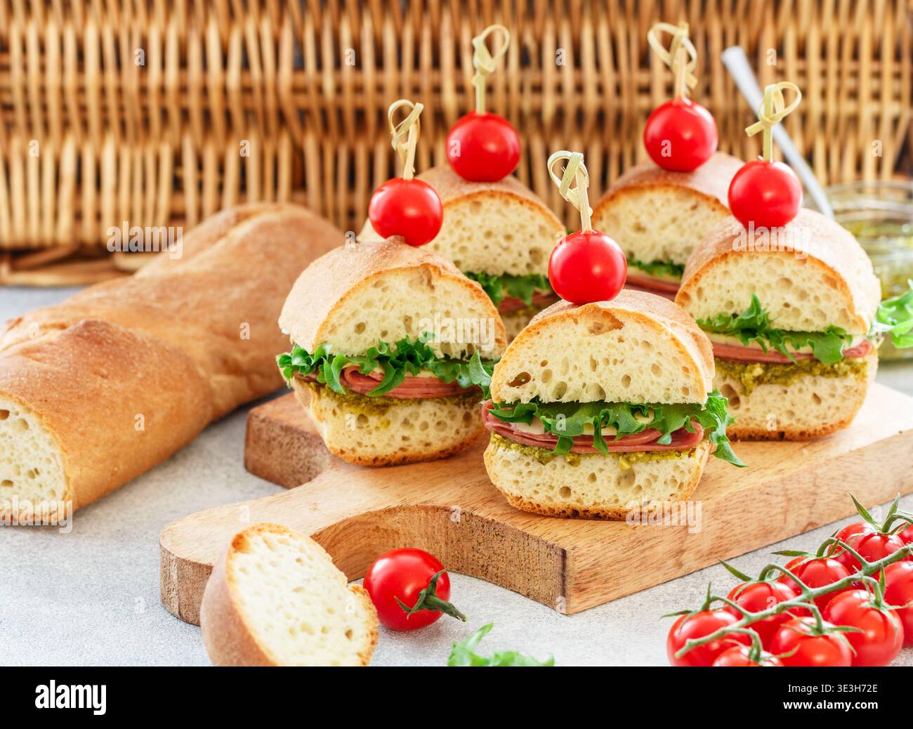 Baguette-Sandwiches mit Pesto-Sauce, Wurst oder Schinken, Käse, Salat und Kirschtomaten. Picknick-Essen. Selektiver Fokus, Kopierraum Stockfoto