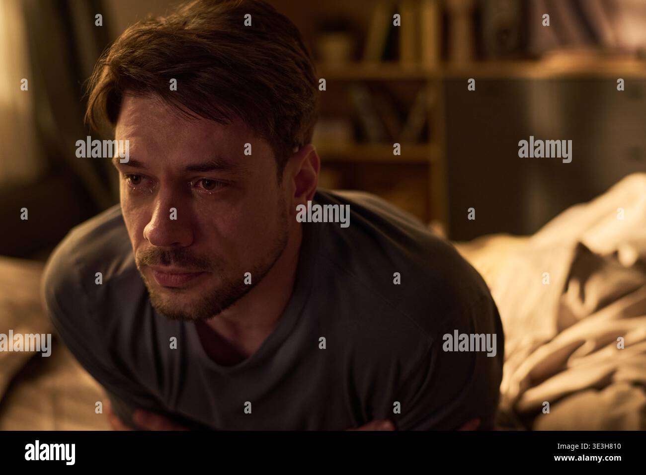 Porträt eines jungen Mannes, der auf dem Bett sitzt und verstört aussieht Stockfoto