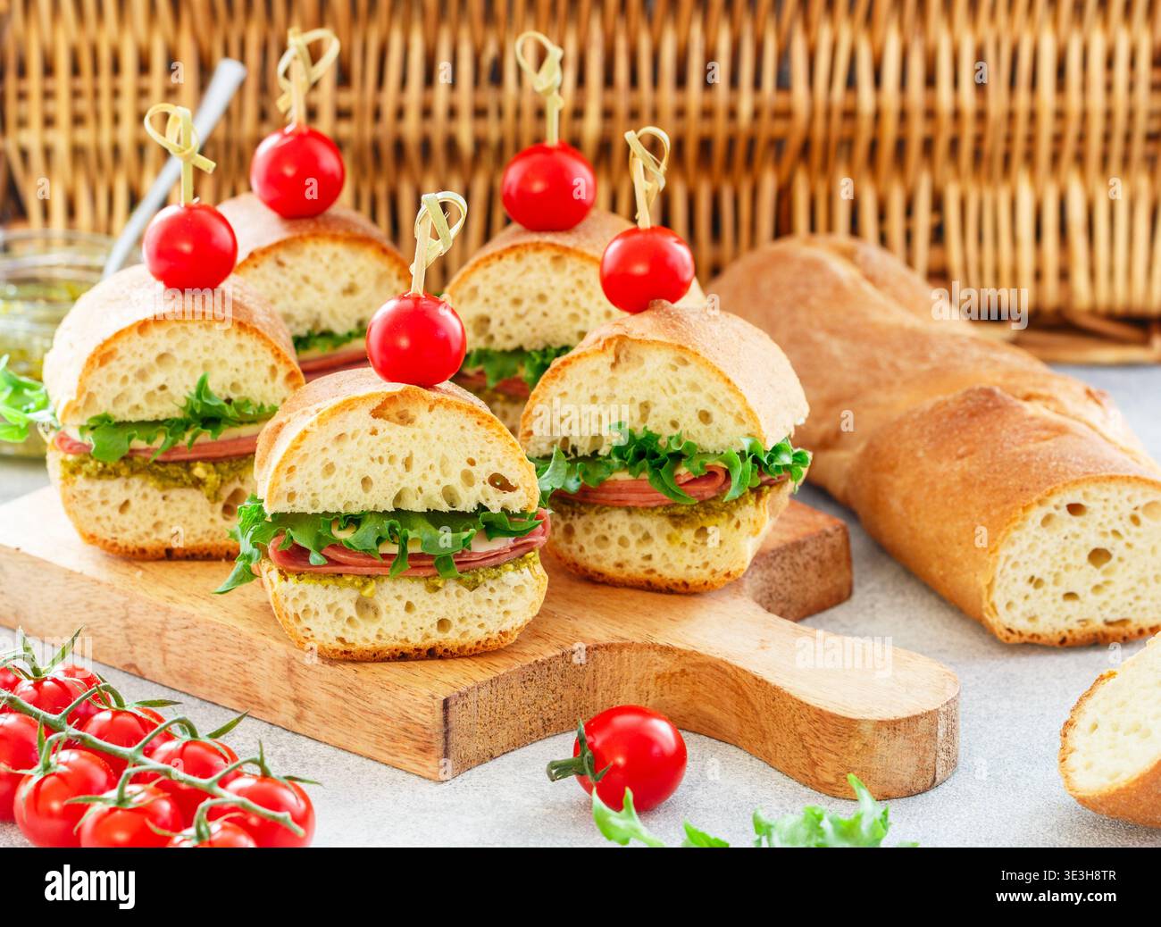 Baguette-Sandwiches mit Pesto-Sauce, Wurst oder Schinken, Käse, Salat und Kirschtomaten. Picknick-Essen. Selektiver Fokus, Kopierraum Stockfoto