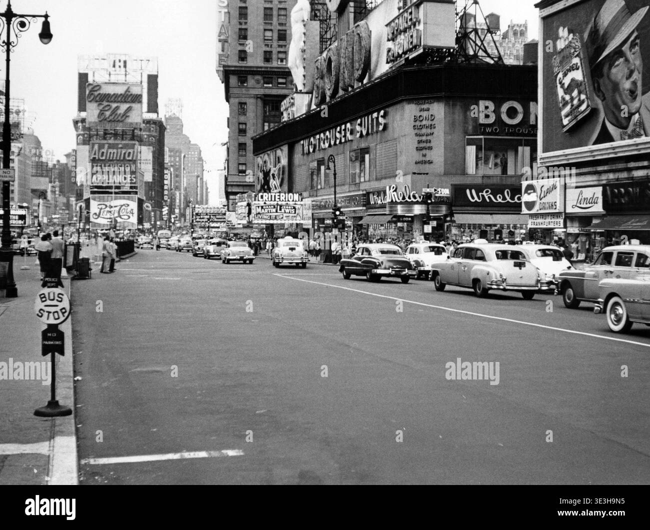 Dieses Schwarz-weiß-Straßenfoto, das Angelo Rizzuto in den 1950er Jahren aufgenommen hat, zeigt die West 45th Street in New York City, voller Oldtimer und Fußgänger. Das prominente Schild des Bond Clothing Store und zahlreiche Werbetafeln, darunter für Fernsehgeräte des Canadian Club und Admiral, verkörpern die lebhafte kommerzielle Atmosphäre des Times Square Mitte des 20. Jahrhunderts. Stockfoto