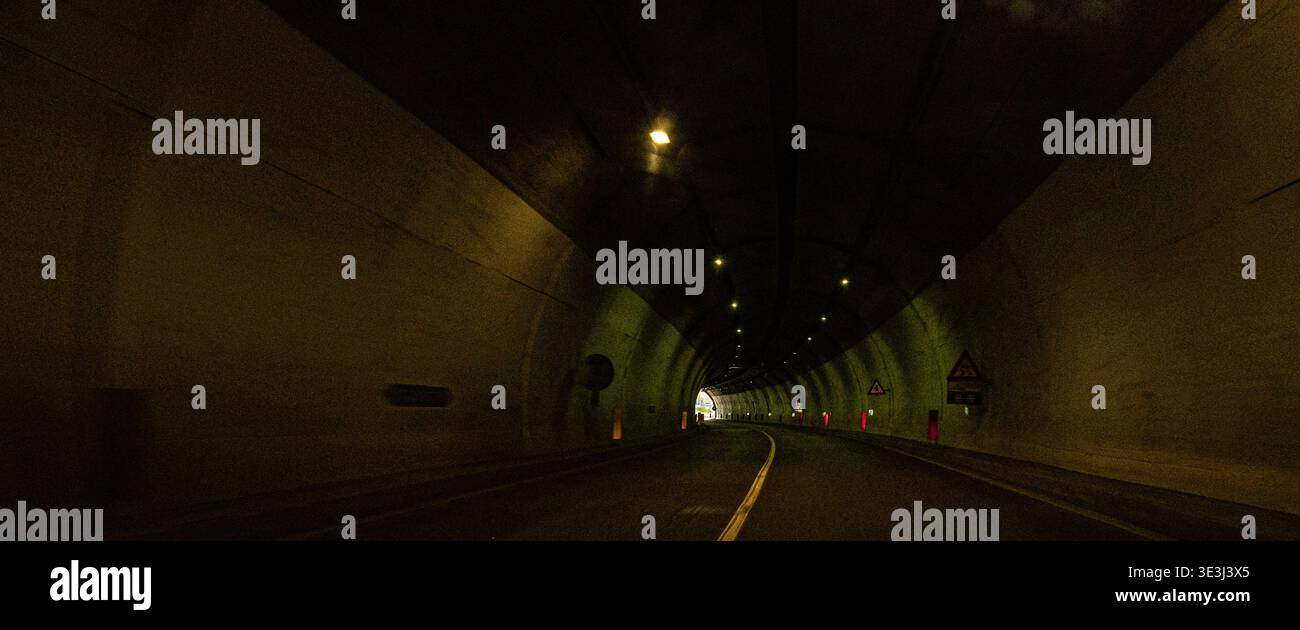 Blick aus dem Innern des Straßentunnels mit grüner Beleuchtung und hellem Licht am Ausgang, zeigt Perspektive auf Reisen, Bewegung und Verkehrsinfrastruktur. Stockfoto